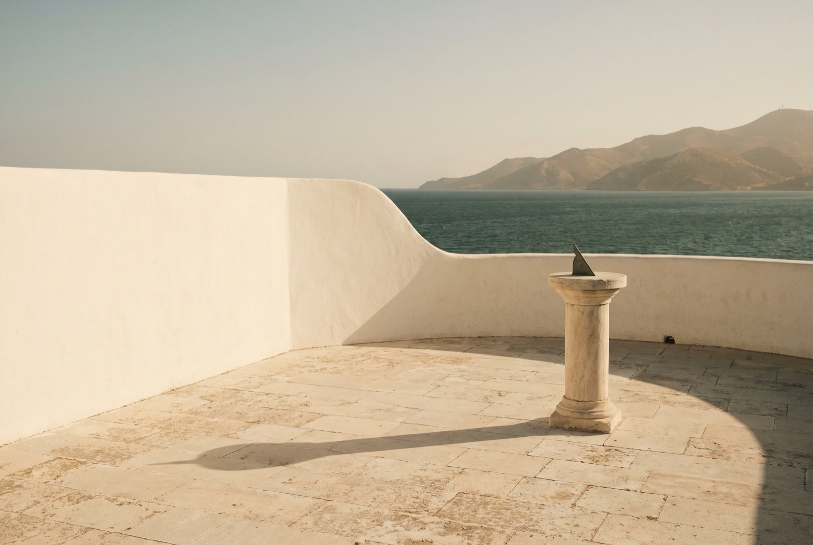 The shadow of a sundial crossing a stone terrace late in the day