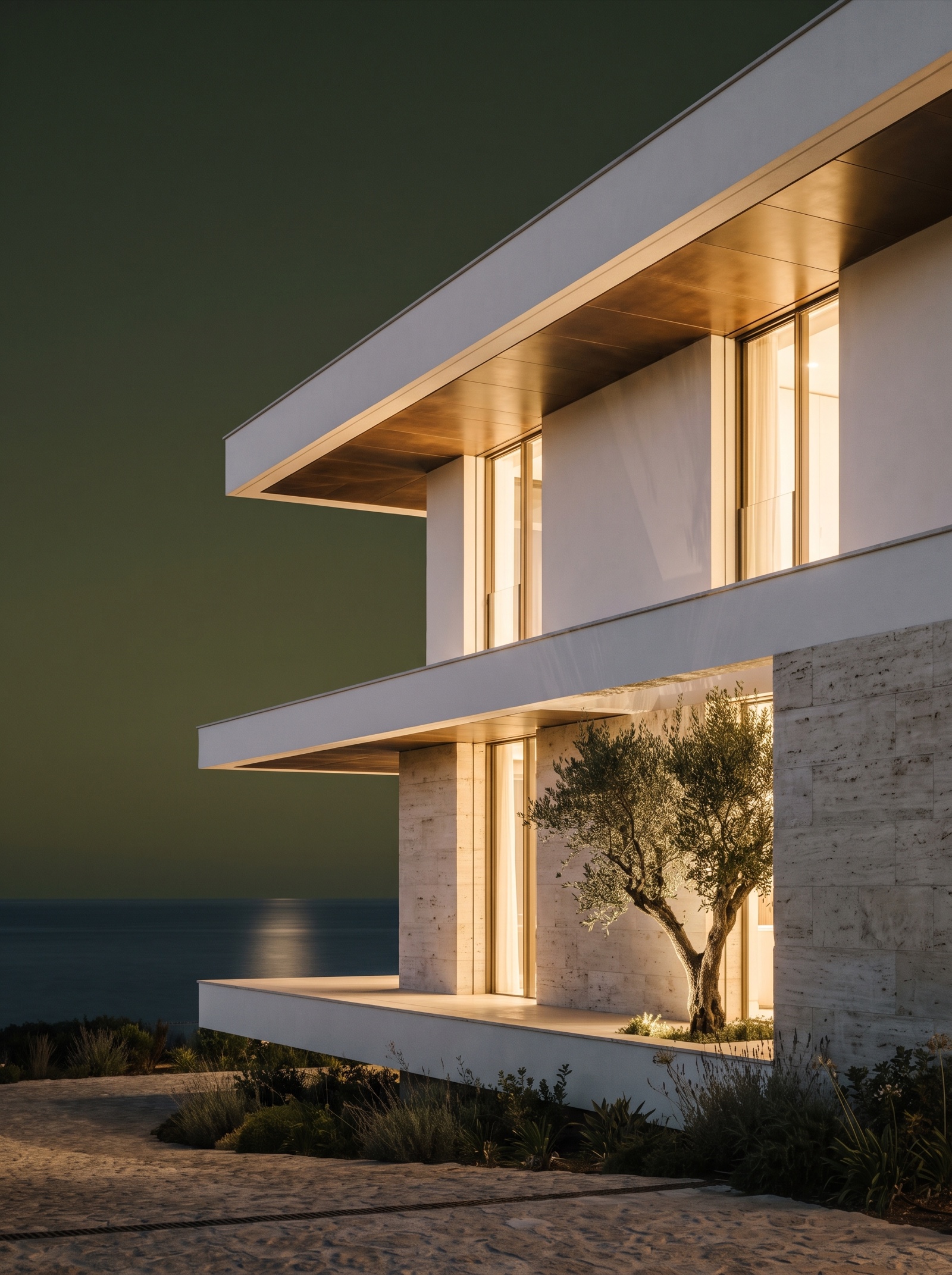 Villa mediterránea contemporánea de noche con la luz cálida del interior encendida, el cielo verde oliva profundo y el mar en calma al fondo.