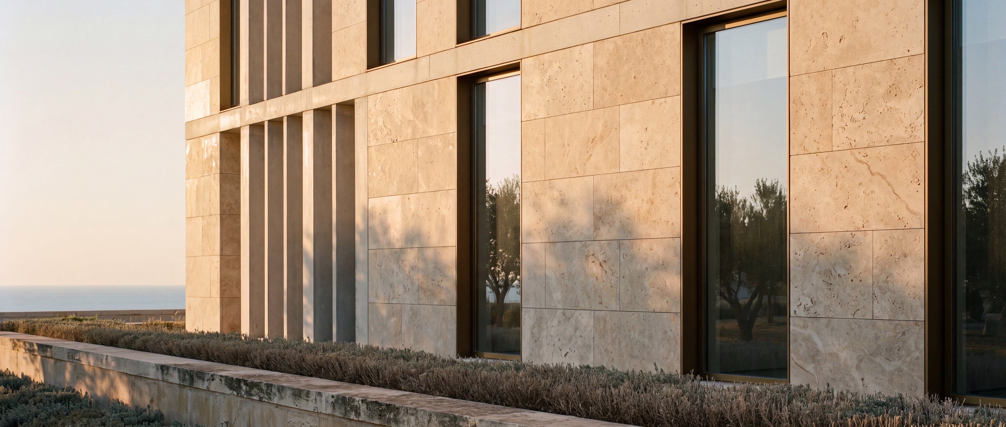 Sede corporativa mediterránea contemporánea en piedra caliza y bronce a la luz del atardecer, con lamas verticales de hormigón y grandes vidrios sin marco.