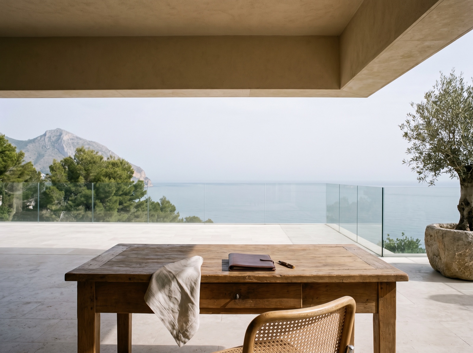 Terraza cubierta de una villa de Marbella: mesa de roble y silla de rejilla a la sombra del voladizo, con el Mediterráneo y Sierra Blanca al fondo